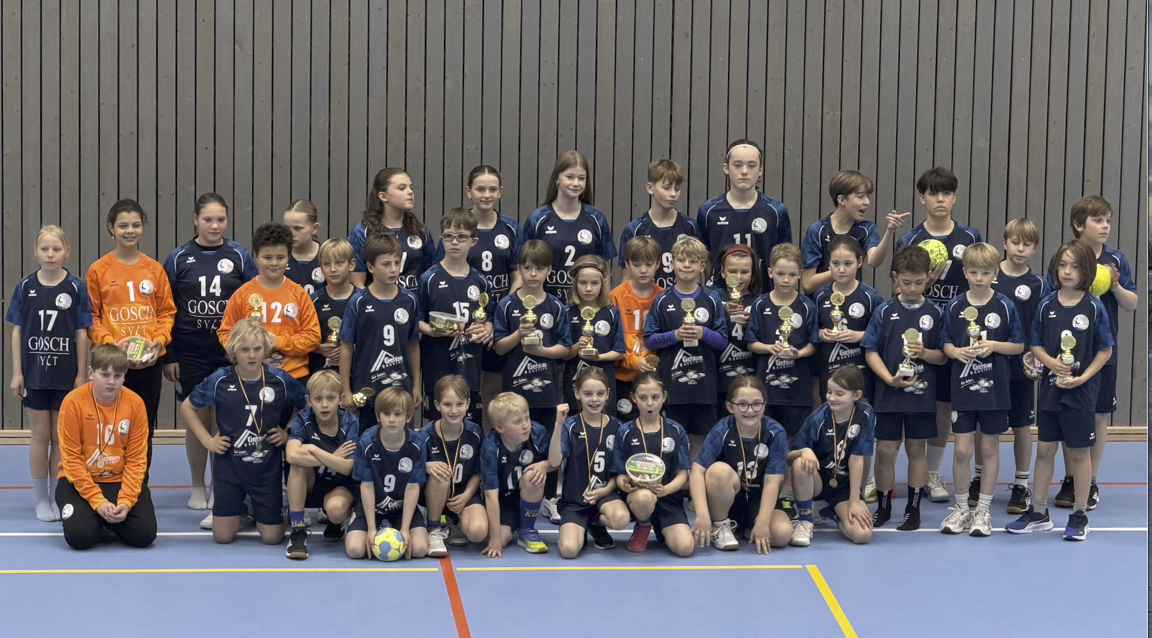 Starker Nachwuchs: Wenn eine Insel wieder an sich glaubt 1 Starker Nachwuchs: Wenn eine Insel wieder an sich glaubt Es gibt Momente im Sport, die größer sind als das Ergebnis auf der Anzeigentafel. Was an diesem Wochenende in der Sporthalle in Tinnum passierte, war so ein Moment. Zwischen den Spielen der Damen- und Herrenmannschaft des TSV Westerland wurden mehrere Jugendteams auf das Parkett gebeten — nicht um zu spielen, sondern um geehrt zu werden. Die F-Jugend mixed, ungeschlagen in dieser Saison, bekam einen Pokal. Die E-Jugend mixed, die männliche und weibliche D-Jugend, die männliche C-Jugend: Sie alle standen vor den Zuschauerinnen und Zuschauern, und der Applaus, der von den Rängen kam, war mehr als höflich. Er war ehrlich. Er war erleichtert. Er trug eine Geschichte in sich, die man kennen muss, um zu verstehen, warum dieser Abend so viel bedeutet. Nicht lange her, dass es anders aussah. Vor einigen Jahren gab es beim TSV Westerland kaum Jugendteams. Kein Nachwuchs, keine Perspektive — und damit genau das Problem, das heute noch sichtbar ist, wenn man auf die Damen- und Herrenmannschaften schaut. Beide Mannschaften warten händeringend auf Spielerinnen und Spieler im Alter um die Achtzehn. Die Generation, die jetzt fehlt, ist jene, die in den Jahren des Stillstands aufgewachsen ist — ohne Angebot, ohne Mannschaft, ohne den Moment, in dem ein Kind zum ersten Mal einen Handball in die Hände bekommt und merkt, dass es das will. Das ist die stille Rechnung, die der Handball auf Sylt noch bezahlt. Und sie macht deutlich, was auf dem Spiel steht — oder besser: was auf dem Spiel stand. Dann haben sich Eltern bewegt. Was folgte, begann unspektakulär. Ein paar Eltern, die sahen, dass nichts passierte, wenn sie nicht selbst anpackten. Eine Mannschaft wurde gemeldet. Dann noch eine. Trainer fanden sich, manche von ihnen selbst Eltern, manche ehemalige Spieler, alle ohne großes Aufheben. Ein Netzwerk entstand — still, praktisch, aus dem Bedürfnis heraus. Heute kümmert sich ein großes Team von Ehrenamtlichen um das, was man von außen gar nicht sieht: die Fahrten, die Hallenzeiten, die Organisation, die Kommunikation, das hundert kleine Dinge, ohne die kein Jugendhandball funktioniert, egal wie gut die Trainer sind. Und die Trainer sind gut. Sie sorgen für die Ausbildung auf dem Platz — für die Technik, das Spielverständnis, den Zusammenhalt. Aber was sie vielleicht am meisten leisten, ist das, wofür es keine Statistik gibt: Sie geben Kindern auf einer Insel das Gefühl, dass ihr Sport hier eine Zukunft hat. Dass es sich lohnt, dabei zu sein. Die Zeichen stehen auf Zukunft. Was in Tinnum an diesem Abend auf dem Parkett stand, ist das Ergebnis von beidem: der Geduld der Trainer und der Begeisterung der Eltern, dem Einsatz der Ehrenamtlichen und dem Mut der Familien, die einfach angefangen haben. Ein Team wurde zu vielen. Eine Idee wurde zu einer Bewegung. Die Damen und Herren, die heute noch auf Nachwuchs warten, schauen auf diese Kinder und wissen: In einigen Jahren werden sie kommen. Nicht alle. Aber genug. Die F-Jugend, die diese Saison kein einziges Spiel verloren hat, ist nicht nur eine Erfolgsgeschichte für ein Wochenende. Sie ist ein Versprechen. Der Handball auf Sylt hat sich seine Zukunft selbst erarbeitet — von unten, mit Ehrenamt und Leidenschaft und dem schlichten Glauben, dass es möglich ist. Das ist selten. Das ist es wert, laut gesagt zu werden.