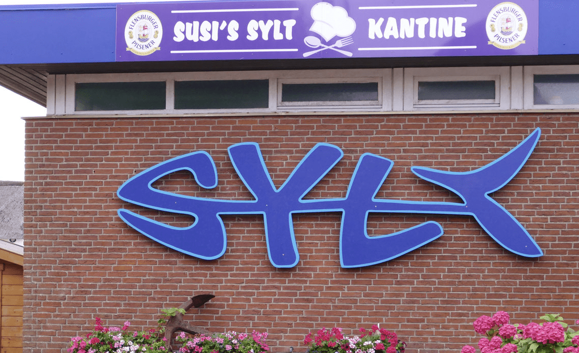 Susi’s Syltkantine: „Futtern wie bei Muttern“ – Ein kulinarischer Streifzug durch die Woche 4 Susi’s Syltkantine: „Futtern wie bei Muttern“ – Ein kulinarischer Streifzug durch die Woche Vergessen Sie Pomp und Schickeria. Wer auf Sylt Hunger nach echter Heimat hat, der steuert direkt in die Keitumer Chaussee. Hier, wo der Kaffee noch ehrlich dampft und die Portionen eine Umarmung auf dem Teller sind, regiert Susi. Ein Blick auf die aktuelle Wochenkarte zeigt: Hier wird noch mit Herz und Hand gekocht. Montag: Kohlroulade „Hausfrauen-Art“ mit Salzkartoffeln Der Wochenstart könnte nicht herzlicher sein. Eine pralle Kohlroulade, gefüllt mit kräftig gewürztem Hackfleisch, sanft geschmort, bis die äußeren Blätter jene wunderbare Süße entfalten. Die dunkle Bratensauce findet in den mehligen Salzkartoffeln ihren perfekten Partner. Ein Gericht, das Kraft für die ganze Woche gibt. Dienstag: Königsberger Klopse in Kapernsauce & Reis Ein Hauch von Nostalgie am Dienstag. Die Klopse sind federleicht und harmonieren tadellos mit der cremigen, hellen Sauce. Die feinen Kapern setzen die nötigen Akzente, während der lockere Reis jeden Tropfen der köstlichen Sauce auffängt. Man fühlt sich sofort an den Küchentisch der Großmutter zurückversetzt. Mittwoch: Deftiges Gulasch „Halb & Halb“ mit Nudeln Zur Wochenmitte wird es rustikal. Zartes Rind- und Schweinefleisch, das fast von selbst zerfällt, badet in einer tiefbraunen, mit viel Liebe gezogenen Zwiebelsauce. Die Nudeln sind der klassische Begleiter, der dieses bodenständige Mahl abrundet. Ein Teller voll Wärme und Zufriedenheit. Donnerstag: Feines Hühnerfrikassee mit Reis Am Donnerstag wird es elegant-bürgerlich. Zartes Geflügelfleisch in einer samtig-weißen Sauce, verfeinert mit Erbsen und Champignons. Das Frikassee bei Susi ist die kulinarische Definition von „Comfort Food“ – leicht genug für den Mittag, aber gehaltvoll genug für echte Genießer. Freitag: Gebratenes Fischfilet mit Remoulade & Kartoffelsalat Traditionell wird die Woche im Norden mit Fisch beschlossen. Goldbraun ausgebacken, saftig im Kern und serviert mit einem Klecks hausgemachter Remoulade. Dazu gibt es den legendären Kartoffelsalat, der genau die richtige Balance zwischen Würze und Cremigkeit trifft. Ein würdiger Abschluss einer schmackhaften Woche. Susi’s Syltkantine – Keitumer Chaussee 6a, Westerland. Wo der Geschmack zu Hause ist.